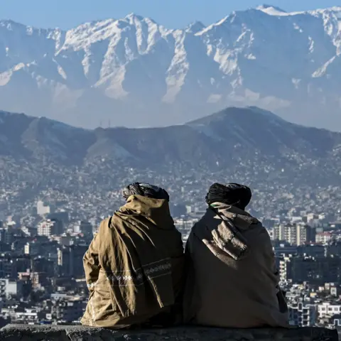 AFP via Getty Images File photo shows two members of the Taliban sitting looking out over the city of Kabul with mountains in the background, they have their backs turned to the camera, taken  at the Wazir Akbar Khan hill in January 2022.