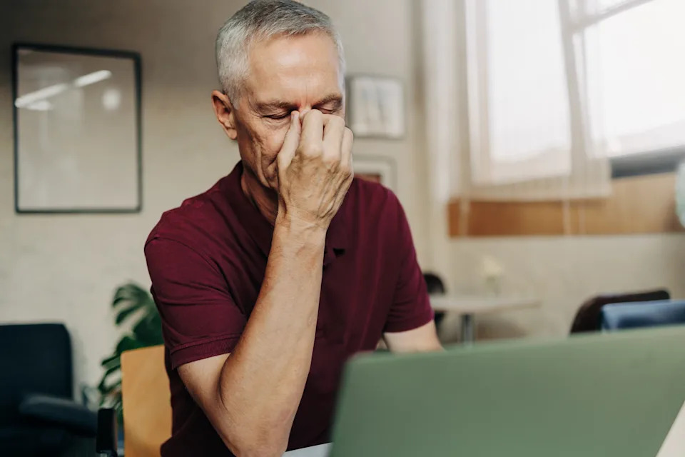 Tired mature man uses laptop