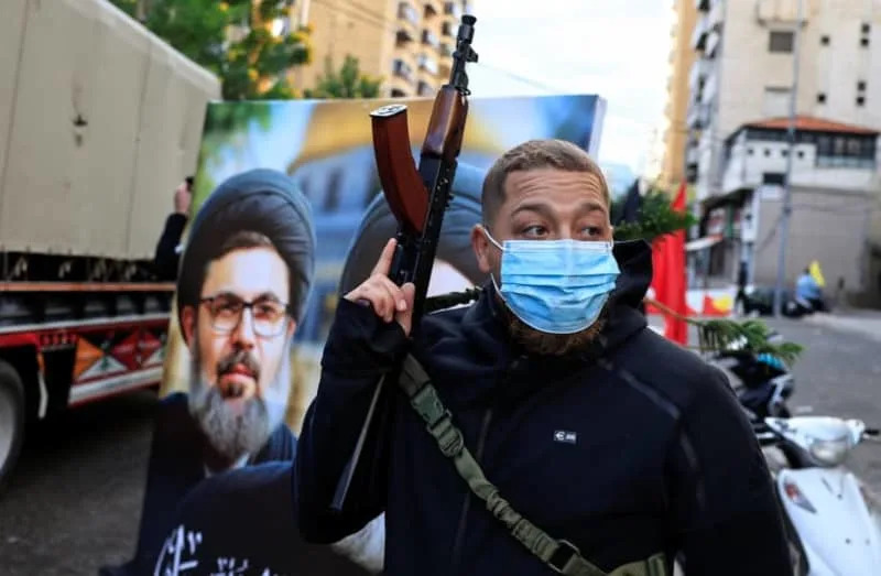 A man holds a weapon next to a poster with an image of late senior Hezbollah official Hashem Safieddine, in Lebanon, November 27, 2024 (credit: REUTERS/THAIER AL-SUDANI)