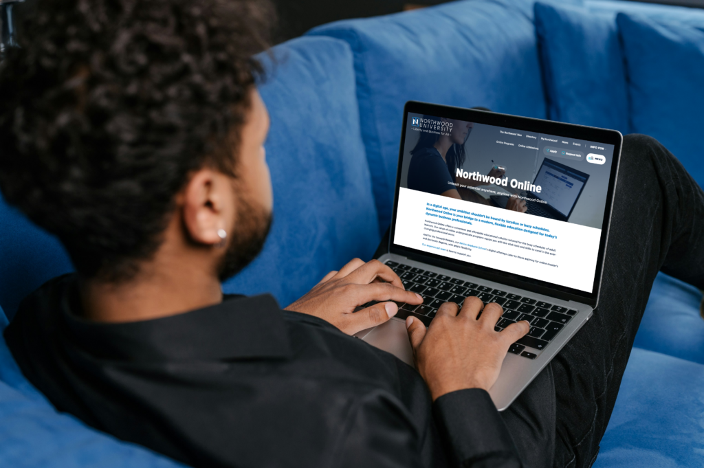 A man sitting on a couch using a laptop, exploring Northwood’s online master’s programs featured in U.S. News & World Report.