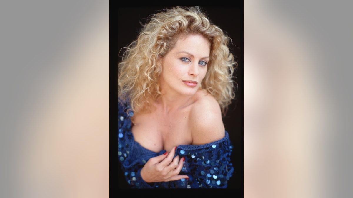 Actress Beverly D'Angelo is shown in a waist-up portrait, wearing a blue shirt and displaying cleavage.