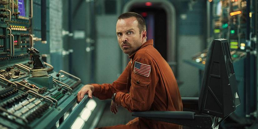 Cliff looks to the side with a quizzical glance while sitting at a control panel in Black Mirror