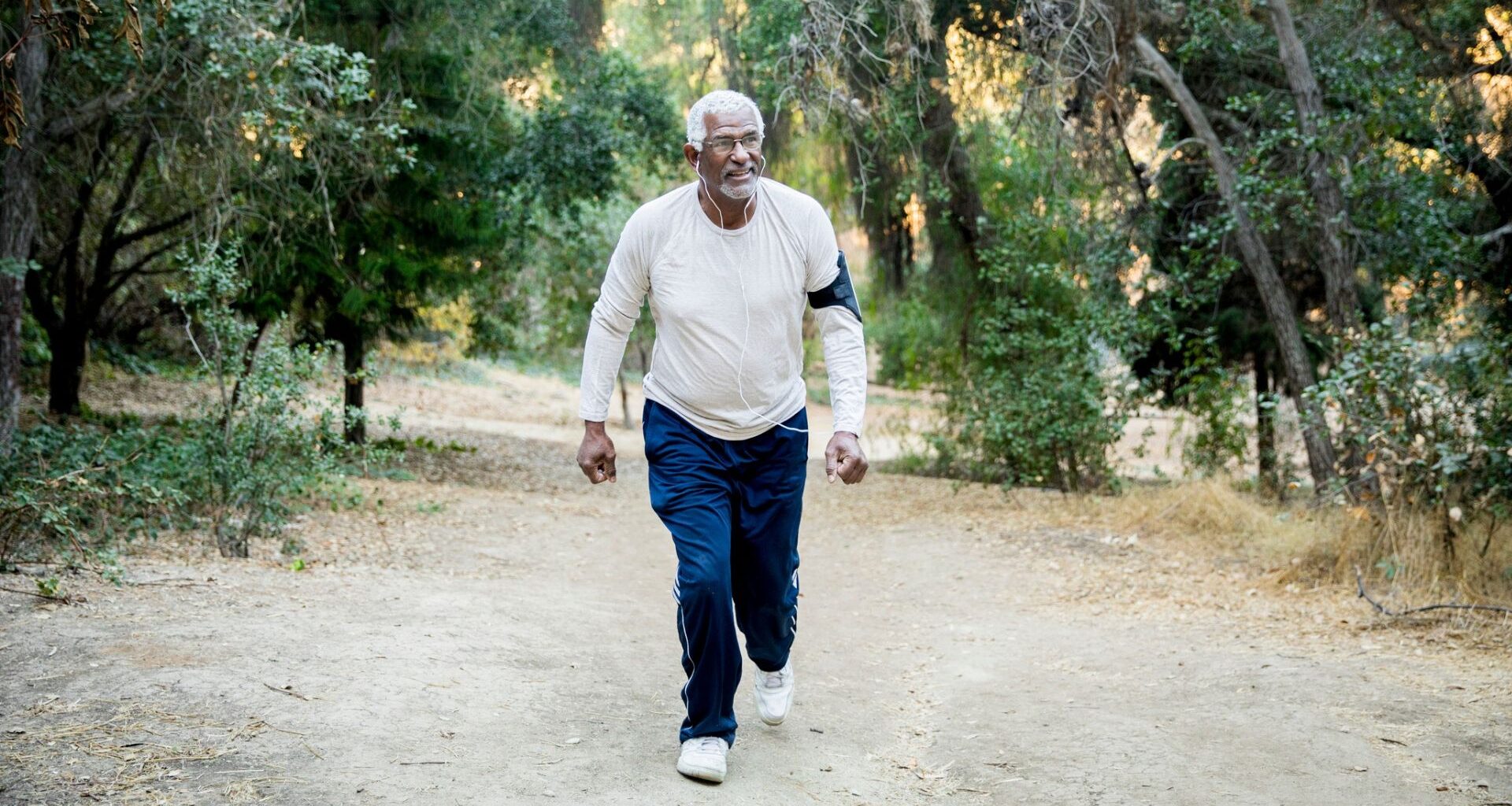 man walking up a bank in a forest, facing the camera wearing a cream sleeved top and navy trousers.