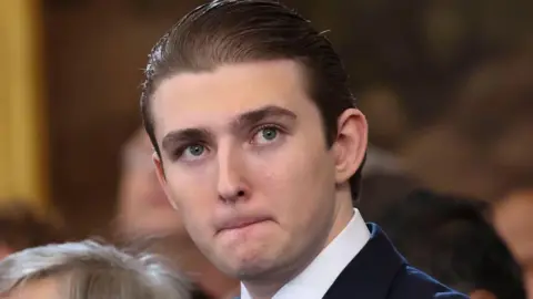 Pool/Getty Images Baron Trump is pictured at his fathers inauguration in the Rotunda of the U.S. Capitol on January 20, 2025.  His hair is slicked back. 