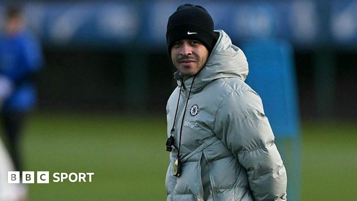 Liam Rosenior, wearing a silver puffer jacket and a black woolly hat and with a whistle and stopwatch around his neck, watches a Chelsea training session