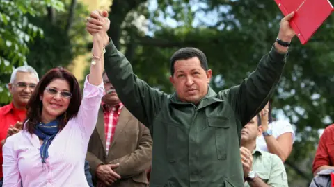 AFP via Getty Images Venezuelan President Hugo Chavez (R) holds up the minutes of the constitutional amendment handed in by the president of the National Assembly Cilia Flores (L).