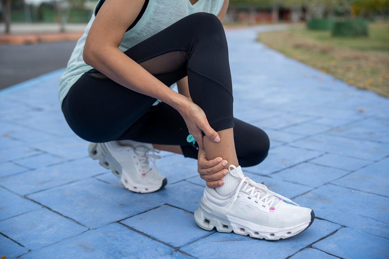 woman holding achilles tendon by hands and suffering with pain. ankle twist sprain accident in sport exercise running jogging. achilles injury on running outdoors.