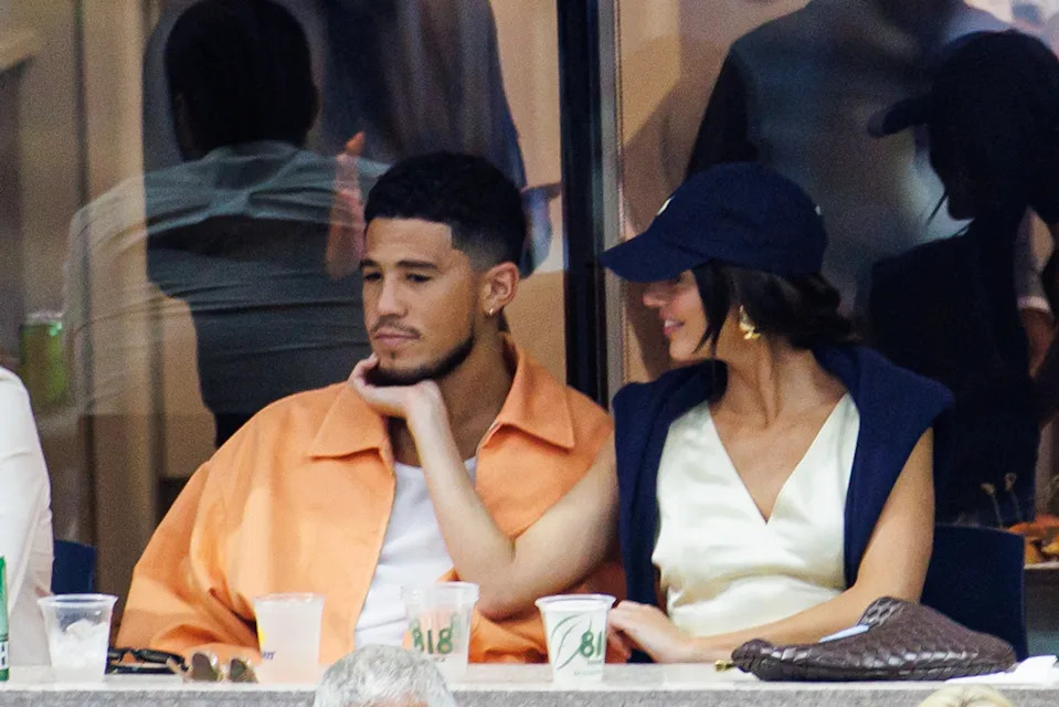 Devin Booker and Kendall Jenner sit together at a sports event as Kendall gently touches his face