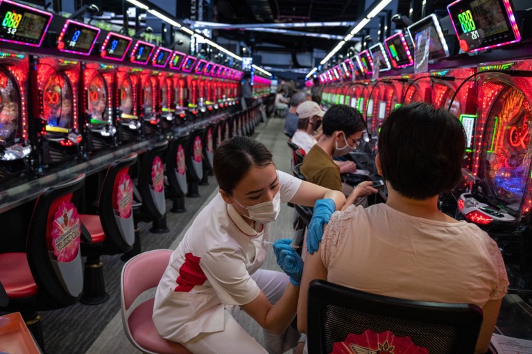 A woman receives a vaccination from a nurse in blue gloves and a face mask in a pachinko parlour in Japan