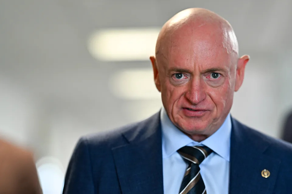 A person in a suit with a striped tie is speaking or making an expression