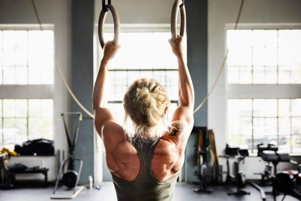 determined female athlete working out on gymnastic rings during cross training session in modern light filled gym