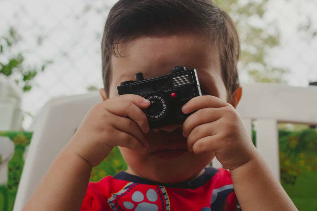 Child boy taking a photo with a vintage camera outdoors.