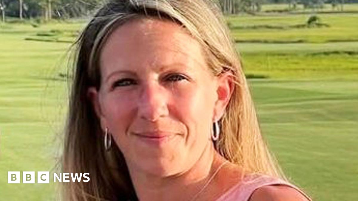 A woman wearing a pink shirt holds a glass while posing in front of a green lawn.