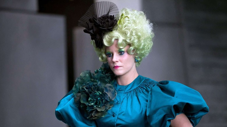 Effie in a green wig and turquoise dress looking stern in The Hunger Games