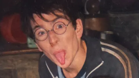 David Holmes David dressed as Harry Potter, wearing glasses and a wig. He has glasses on and is sticking his tongue out.