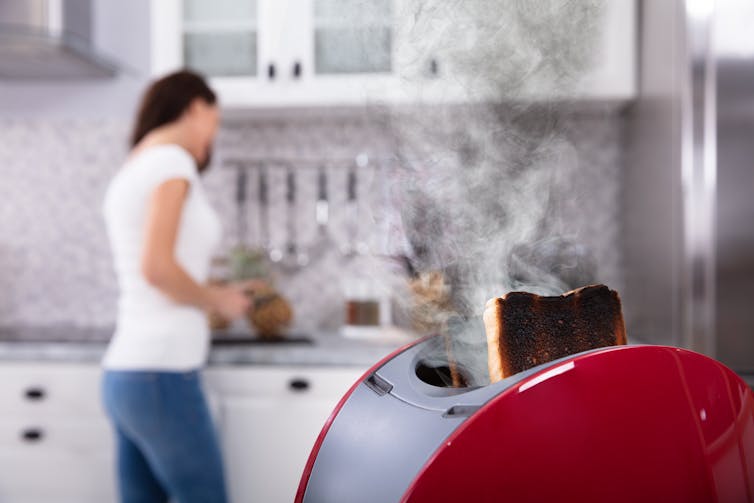 toast burning in red toaster, woman in background in modern kitchen