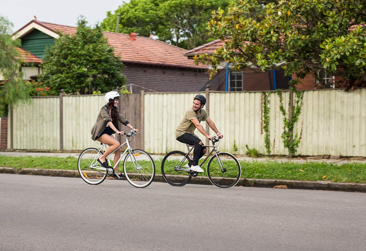 A man and woman riding their bikes down a suburban street.