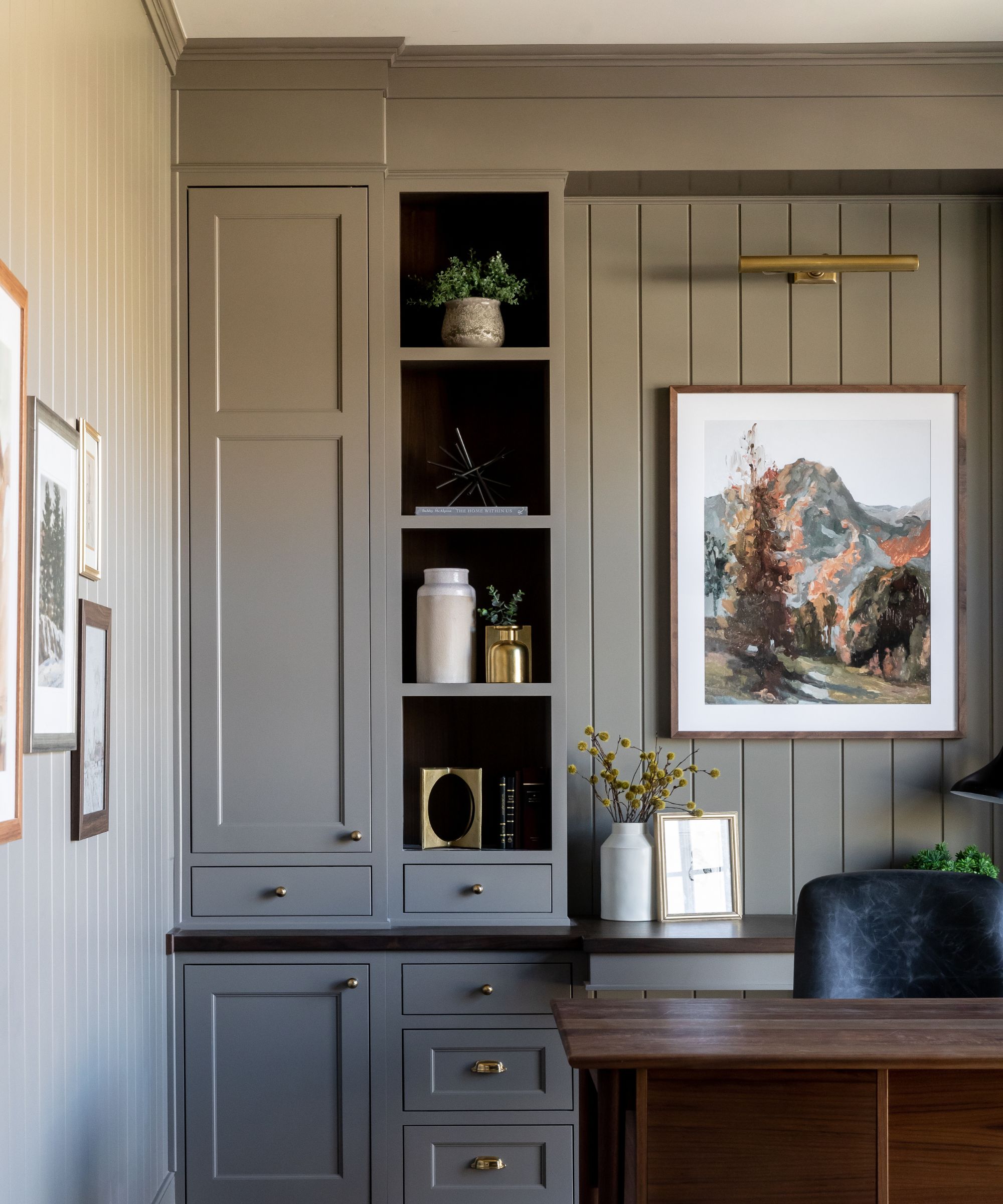 A home office painted dark green with built-in storage and display shelves