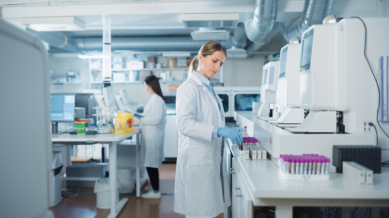 woman scientists working in a lab environment, vials and computer machines visible on tables