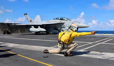 A U.S. Navy F/A-18F Super Hornet prepares to launch from the USS Gerald R. Ford as a crew member in a yellow shirt signals on the flight deck.