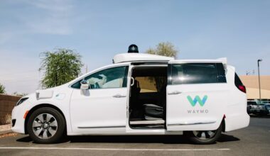 A Waymo Chrysler Pacifica autonomous minivan is parked with its sliding door open, showing the empty passenger seat.