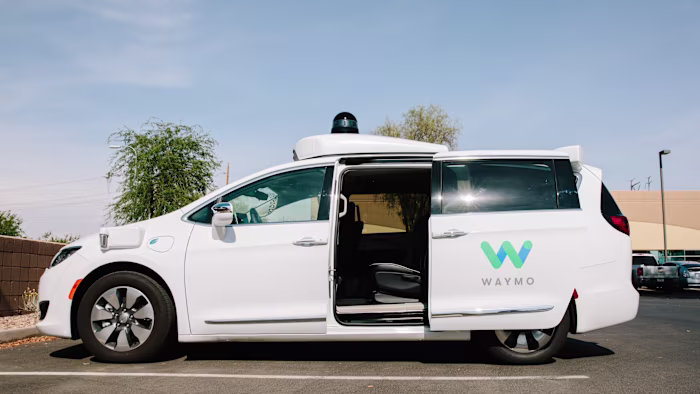 A Waymo Chrysler Pacifica autonomous minivan is parked with its sliding door open, showing the empty passenger seat.