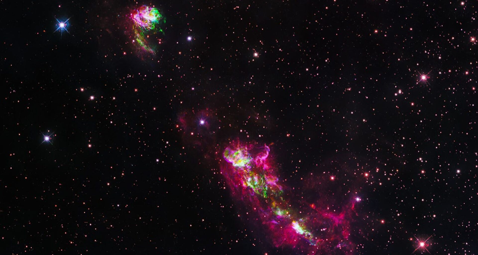 Narrow, knotted clouds of purple and green glowing gas are seen against a field of stars. Some of the larger stars have diffraction spikes.