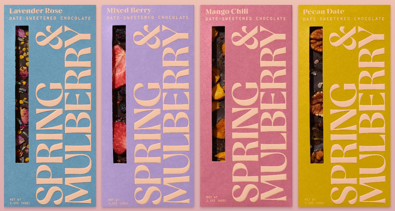 Four colorful chocolate bar packages labeled "Spring & Mulberry" in bold text, featuring flavors: Lavender Rose, Mixed Berry, Mango Chili, and Pecan Date, each with a peek-through window showing the chocolate inside.