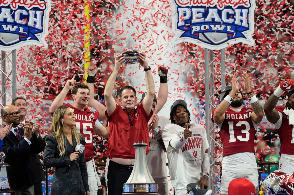 Indiana head coach Curt Cignetti holding up the Peach Bowl trophy after winning the game.