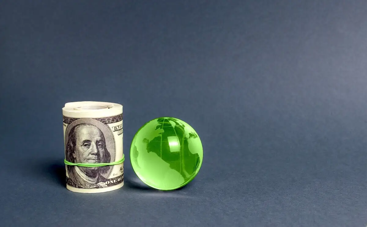 Roll of $100 bills next to a green world globe