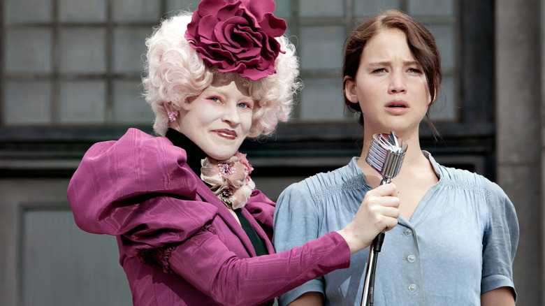 Effie holding the microphone up for Katniss in The Hunger Games