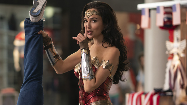 Gal Gadot as Wonder Woman with her finger up to her mouth holding someone upside down in Wonder Woman 1984