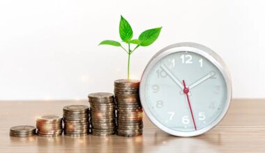 Vertical stacks of coins growing in size from left to right on a wooden surface with a plant growing out of the top of the tallest stack; a clock is pictured next to the coins