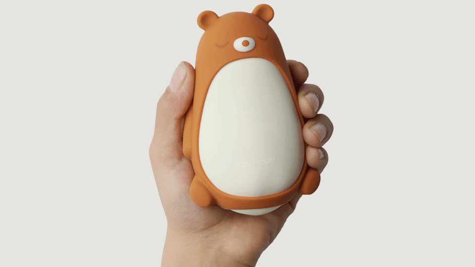 A hand holds the Moonbird Moonbuddy. The device has the teddy sleeve on. 