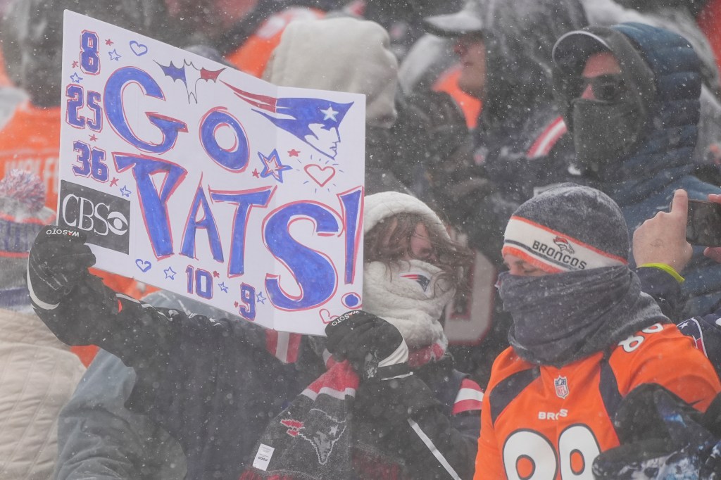 New England Patriots fan cheers next to a Denver Broncos fan during an NFL football game.