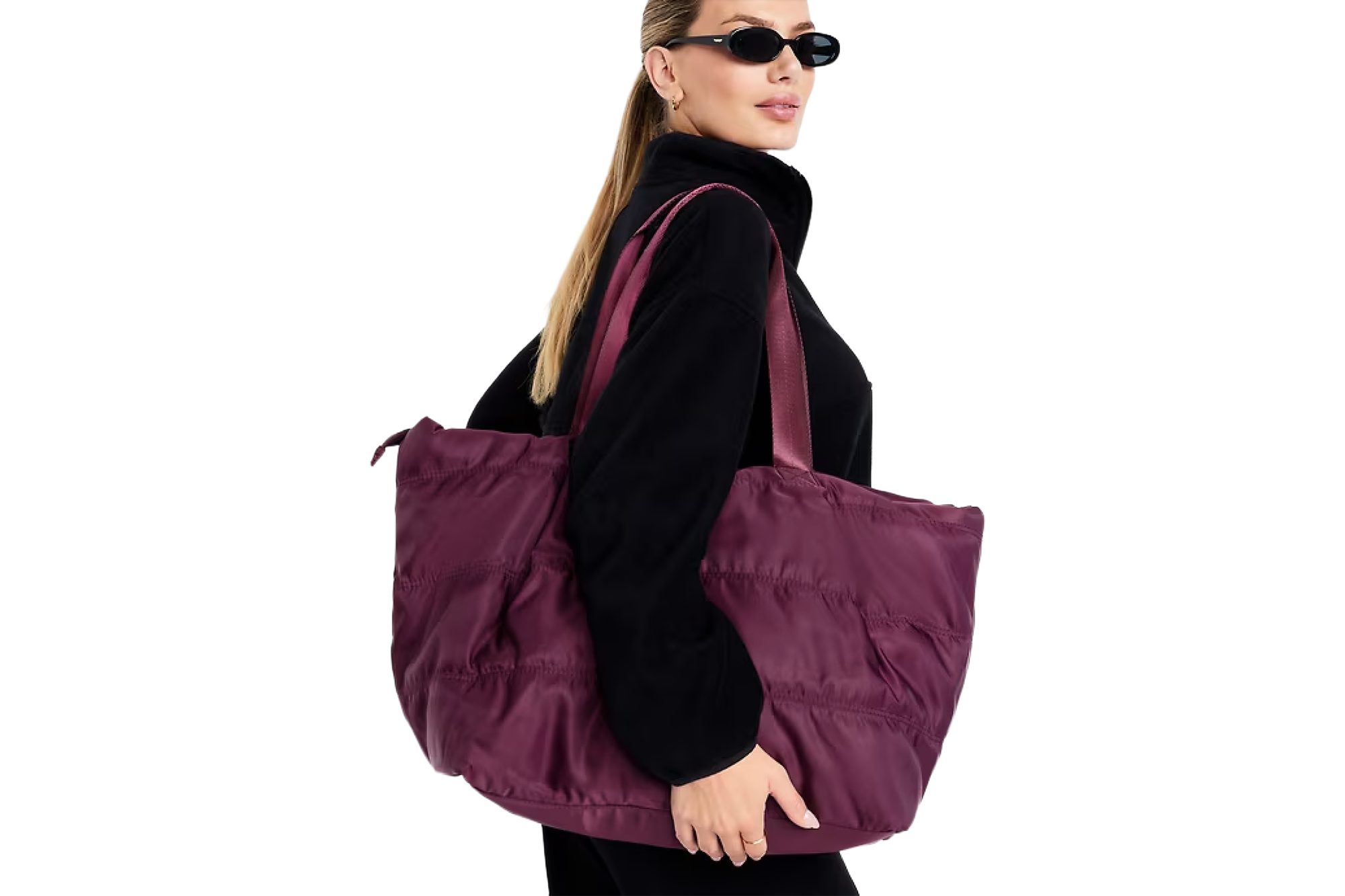 A woman wearing black sunglasses and a black top carrying a purple quilted tote bag.