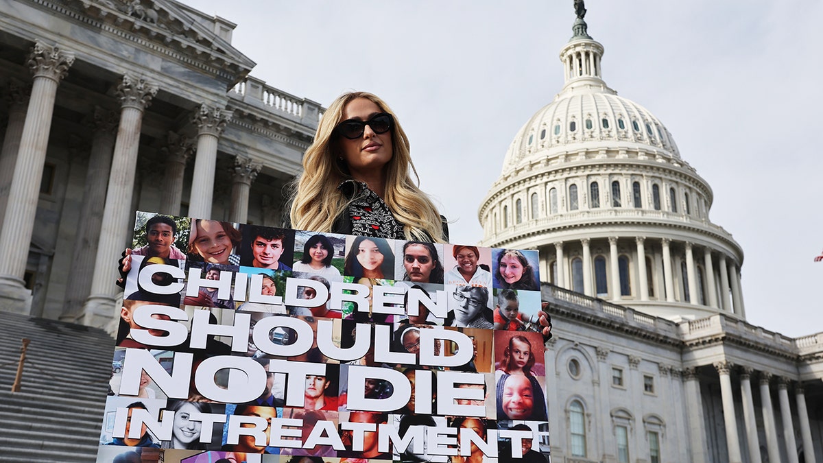 Paris Hilton holding a poster advocating against childhood abuse on Capitol Hill.