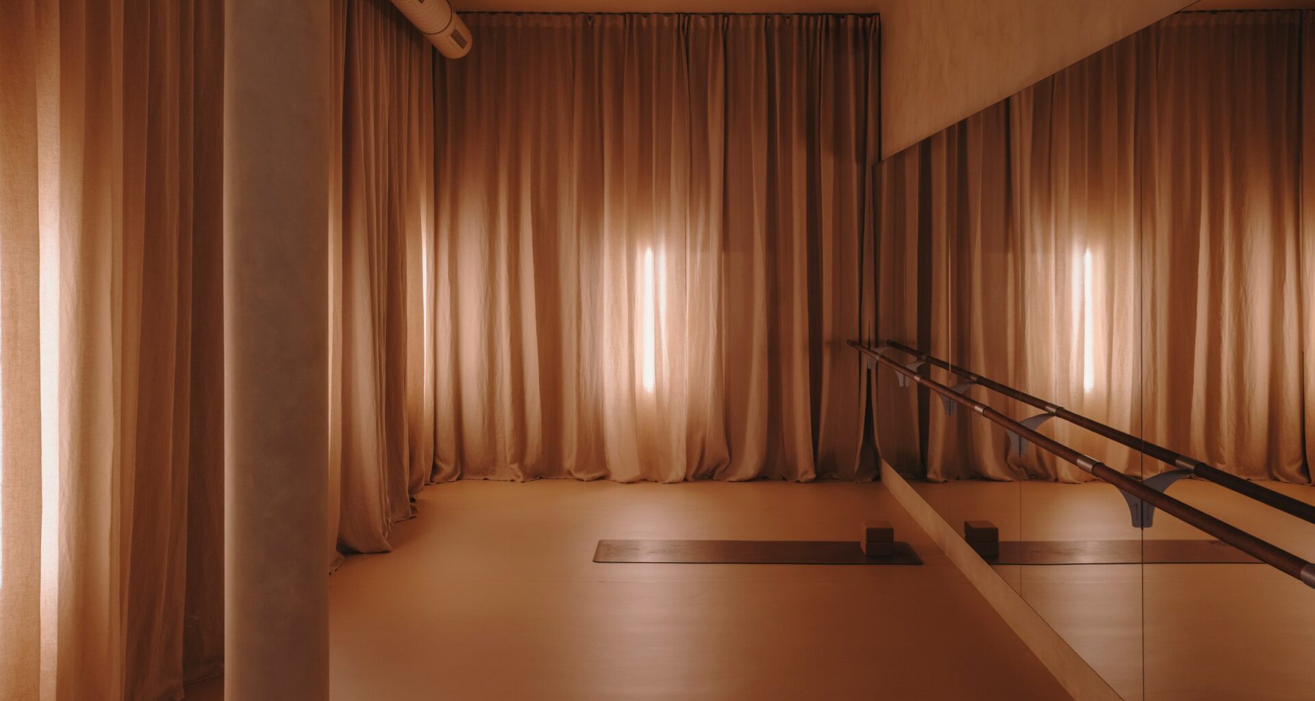 Barre studio with floor-to-ceiling curtains and mirrored walls