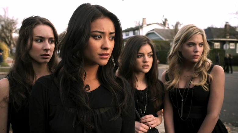 Troian Bellisario as Spencer, Shay Mitchell as Emily, Lucy Hale as Aria, and Ashley Benson as Hanna, standing in black dresses in Pretty Little Liars