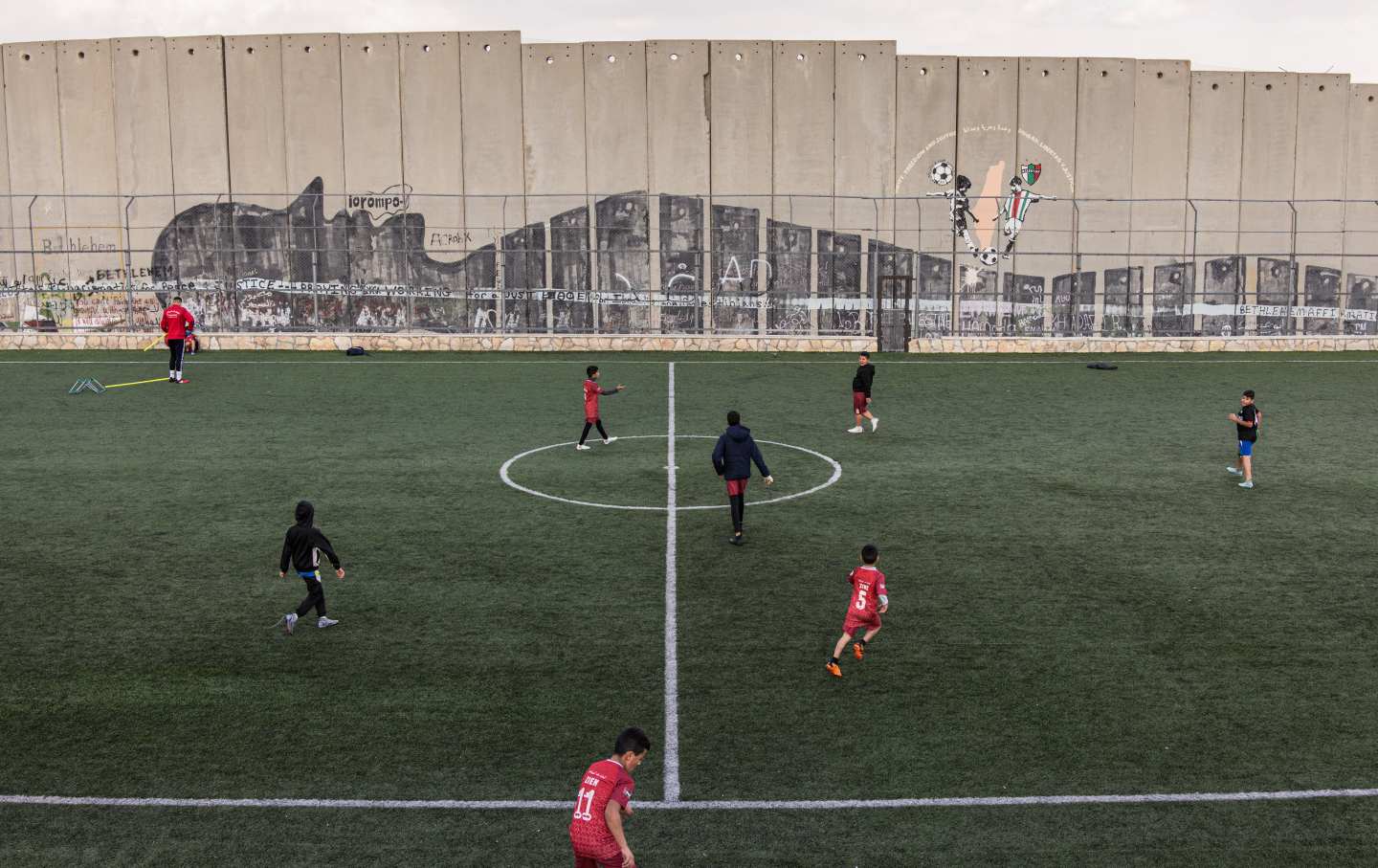 Displaced Palestinian youths take part in a training session at the Aida Refugee Camp's football pitch, next to the separation wall outside Bethlehem in the occupied West Bank, on December 16, 2025, a few weeks after an Israeli military decision to demolish the field.