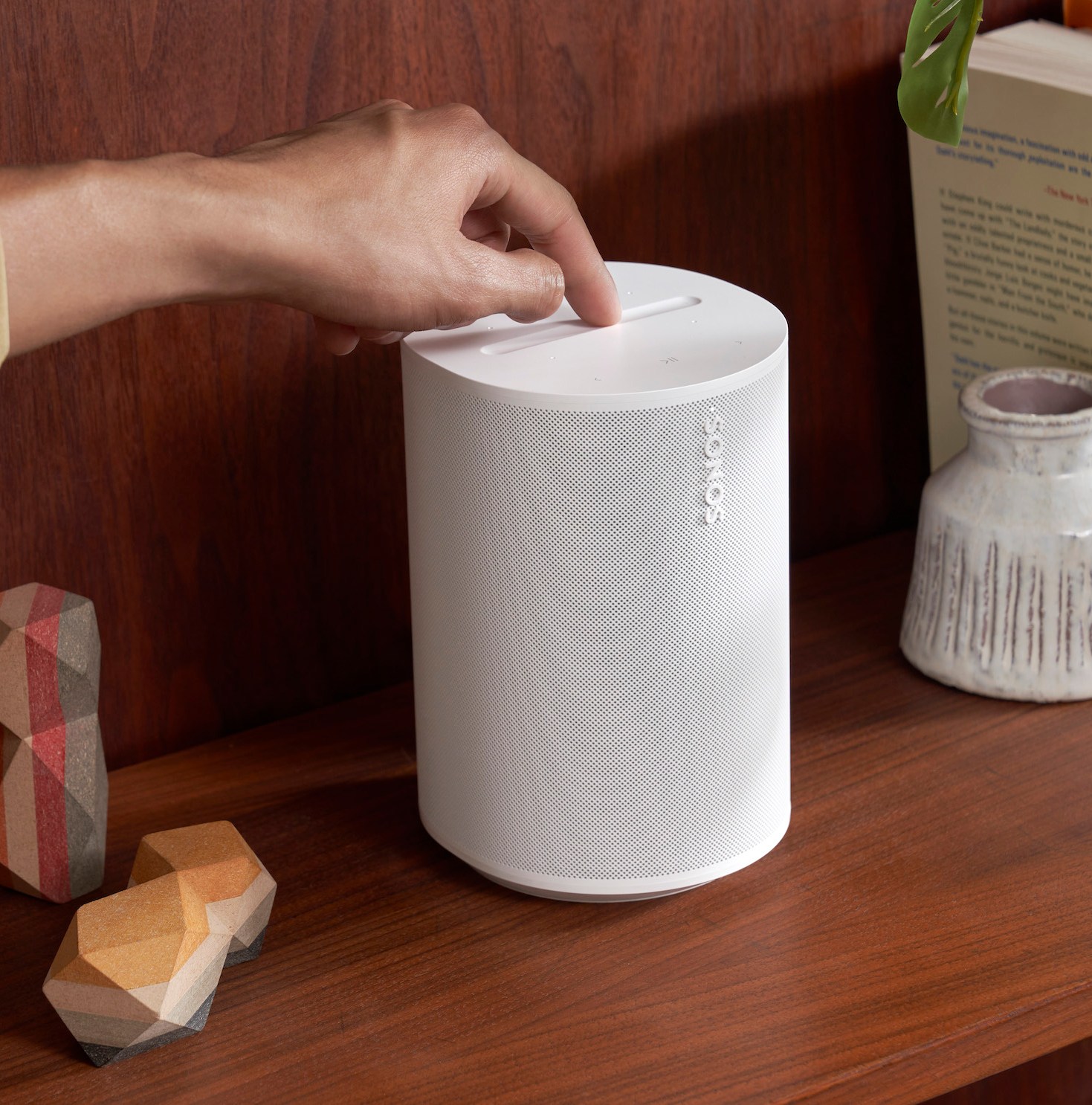 A marketing image of the Sonos Era 100 speaker on a wood shelf.