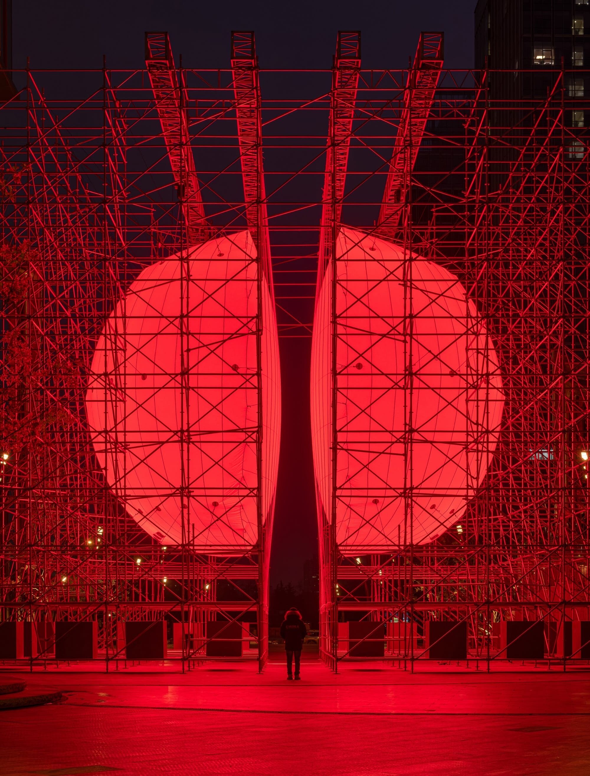 A large-scale installation by SpY of two glowing, red half-spheres within a metal framework