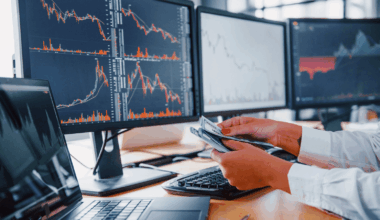 Photo of a person counting money in front of multiple stock charts