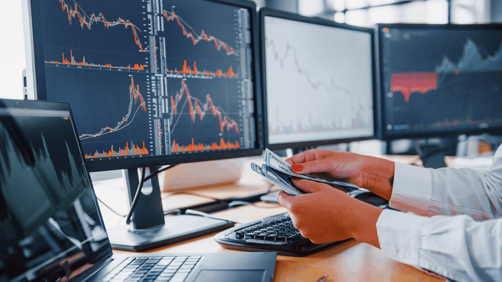 Photo of a person counting money in front of multiple stock charts