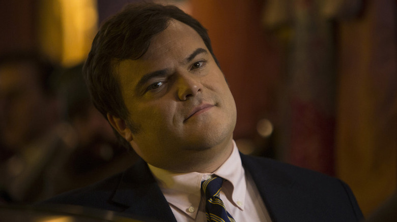 Alex Talbot (Jack Black) smugly leans back while seated in The Brink