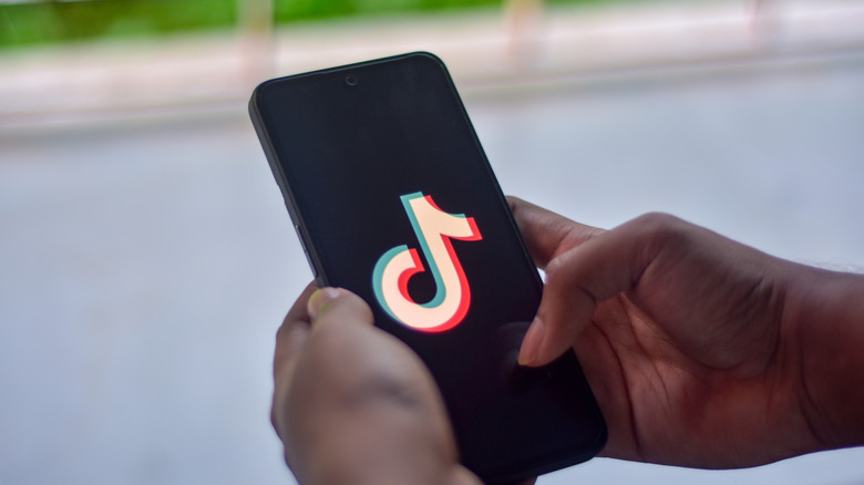 Hand holding a phone displaying TikTok app logo