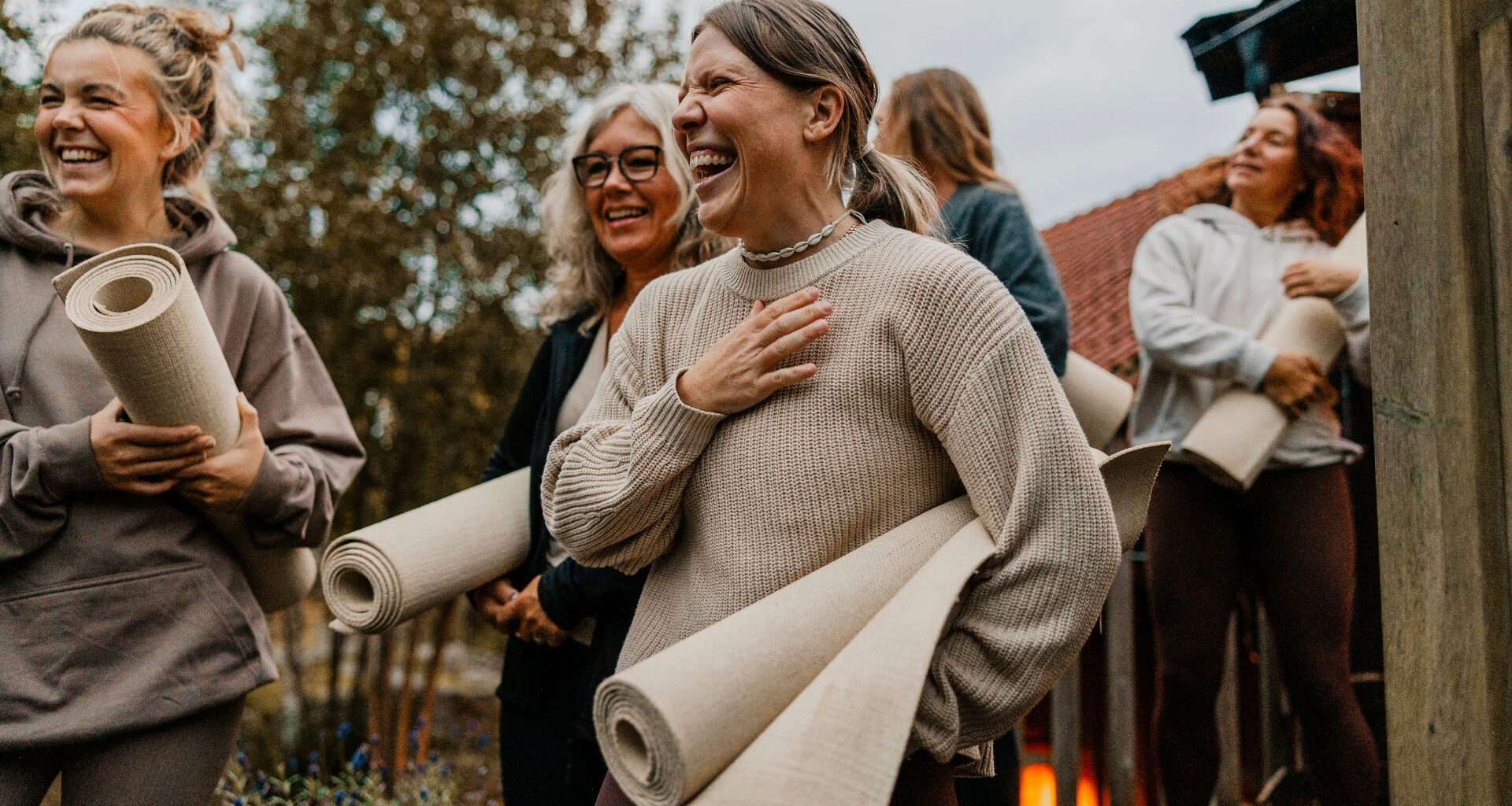 Women laughing together, holding yoga mats in hand outdoors