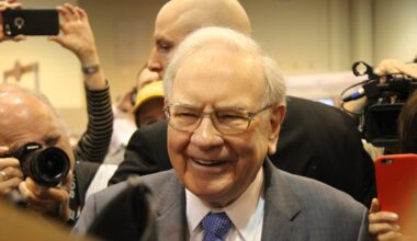 Warren Buffett smiling, surrounded by cameras.