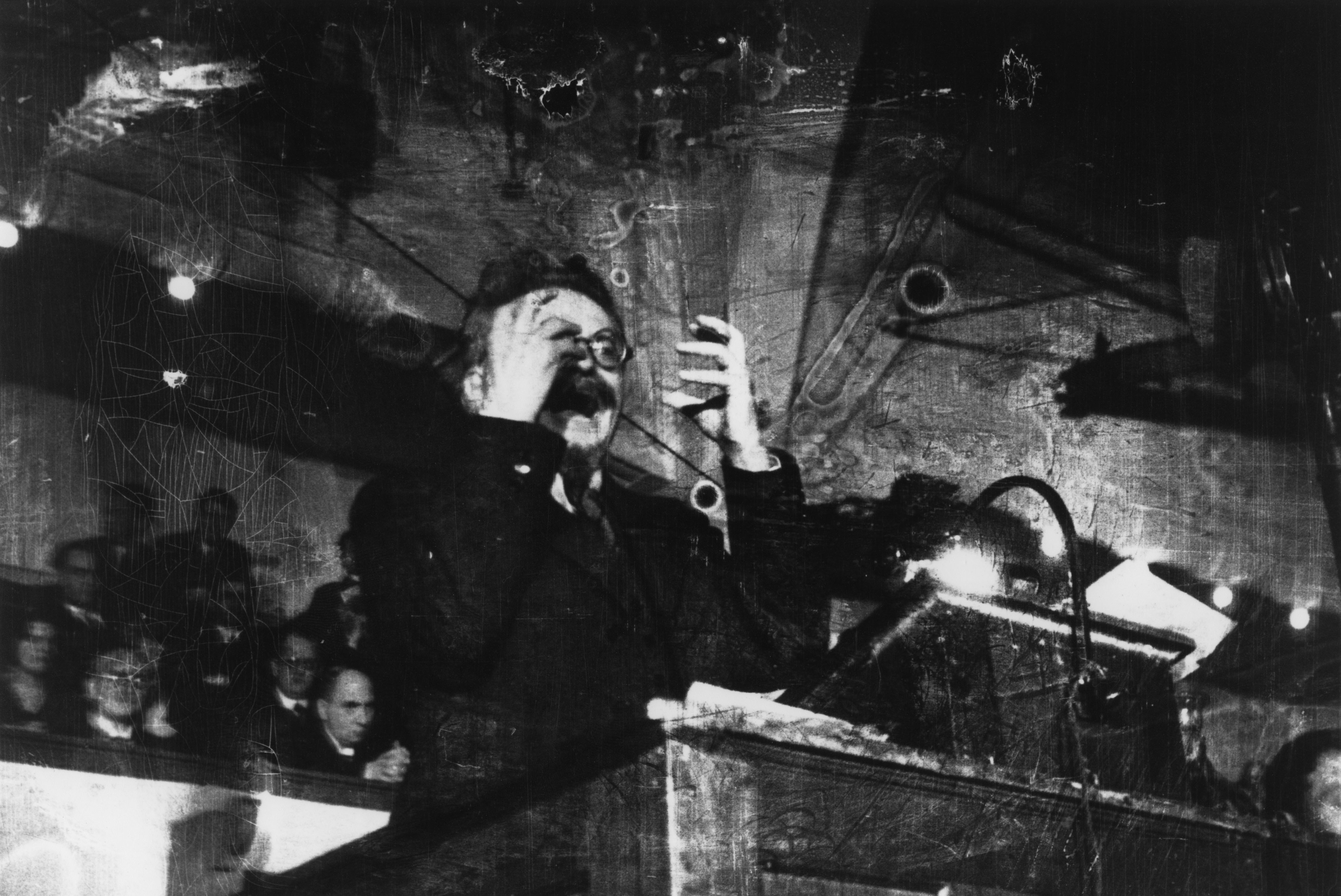 Leon Trotsky lecturing, captured in a black and white photograph with visible imperfections.