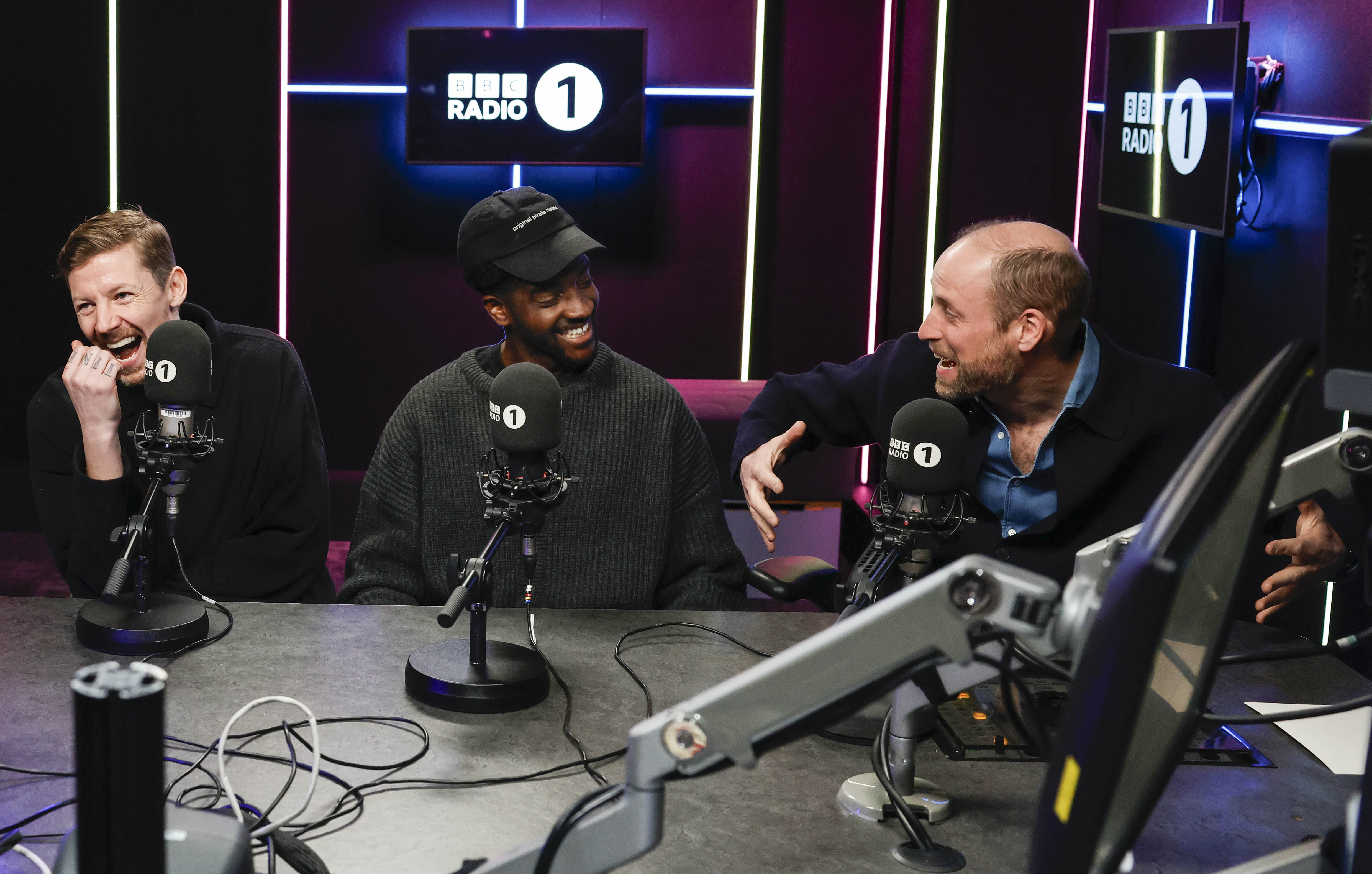 Prince William and two men laughing in a recording studio with "BBC Radio 1" logos visible.